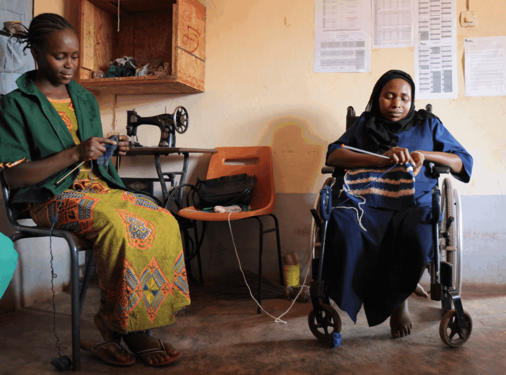 Deux femmes tricotent ensemble dans un atelier, l’une assise, l’autre en fauteuil roulant.