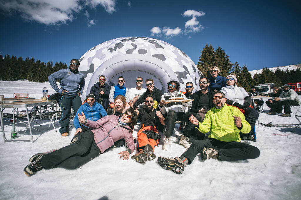 Groupe de personnes souriantes posant ensemble au soleil dans la neige devant une tente gonflable.