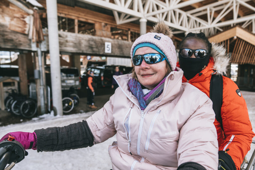 Deux femmes en tenues de neige et lunettes de soleil sourient, assises l'une dernière l'autre sur une motoneige.