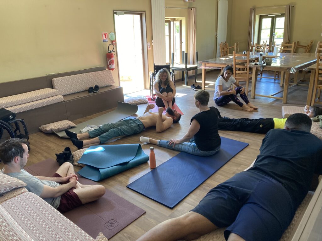Groupe de personnes participant à une séance de mobilité douce dans une salle lumineuse, assises ou allongées sur des tapis de yoga, dans une ambiance conviviale et détendue.