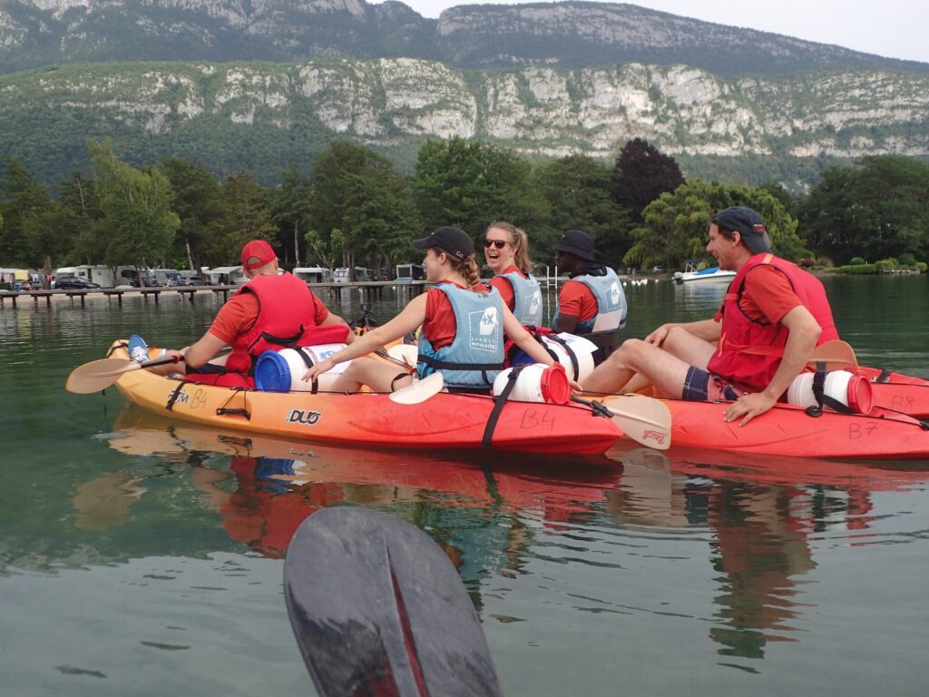 Groupe de participants en situation de handicap et valides pagayant ensemble en kayak sur le lac d’Annecy, entouré de montagnes verdoyantes.
