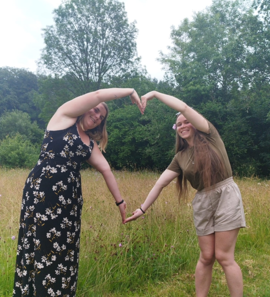 Julie et Romane, de l'antenne des Pays de la Loire, debout dans l'herbe, forment un coeur avec leurs bras levés