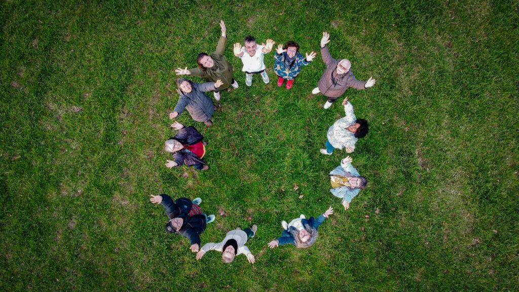  Vue aérienne d’un groupe de personnes formant un cercle sur une pelouse verte, levant les bras et souriant vers le ciel.