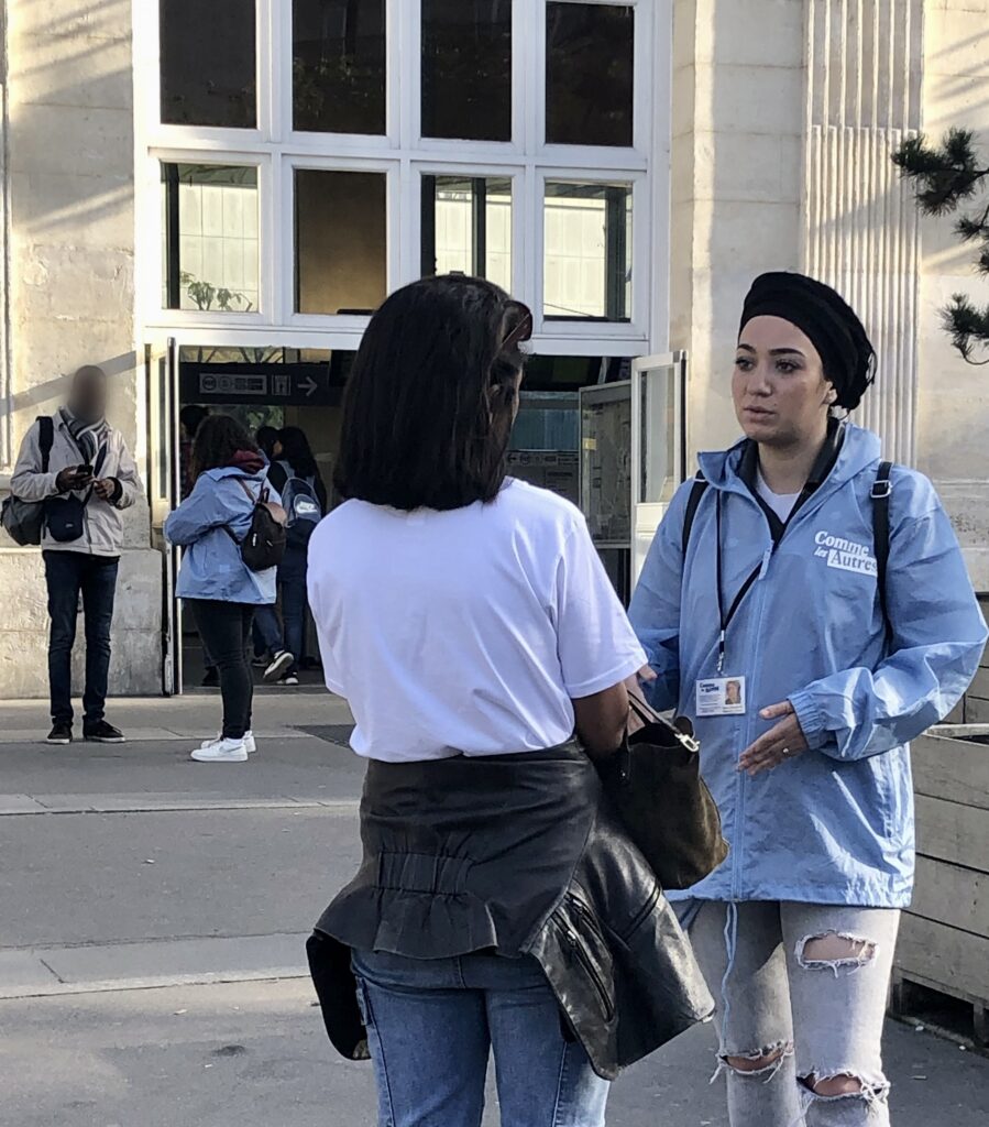 Une intervenante de l’association Comme Les Autres échange avec une femme devant une gare parisienne, dans le cadre de la collecte.