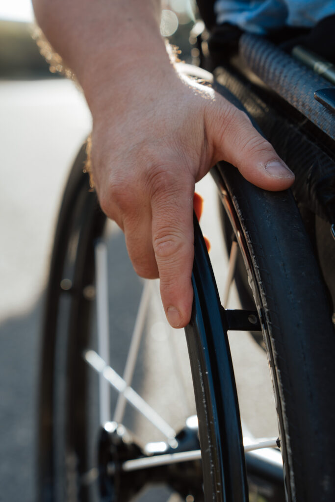 Main d’une personne posée sur la roue d’un fauteuil roulant, éclairée par la lumière naturelle.